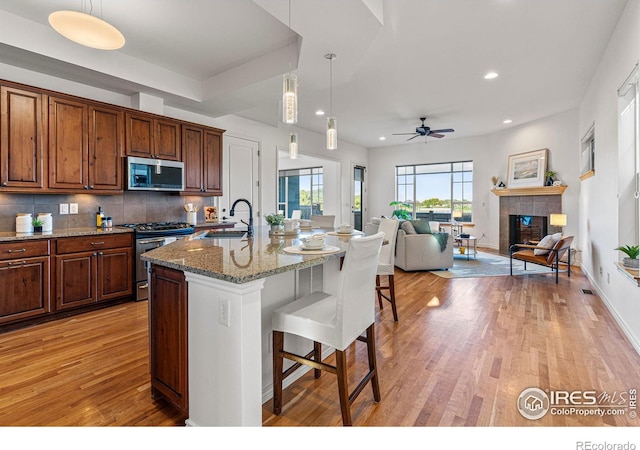 kitchen featuring ceiling fan, sink, stainless steel appliances, a breakfast bar, and a fireplace