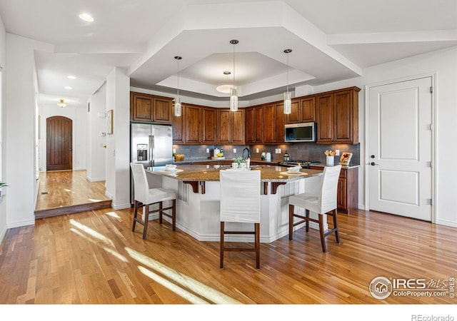 kitchen featuring light stone counters, light hardwood / wood-style flooring, backsplash, stainless steel appliances, and a kitchen breakfast bar