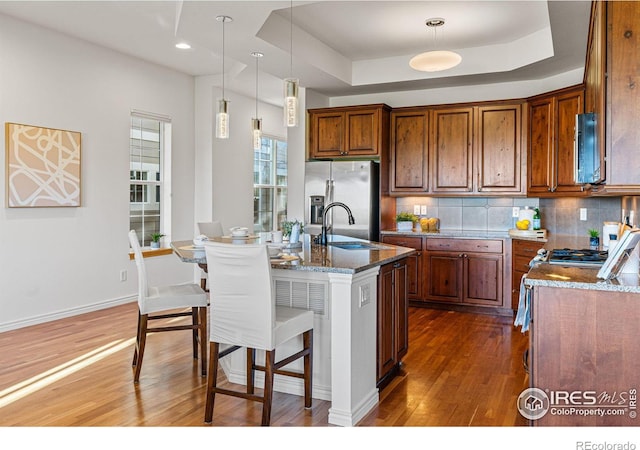 kitchen featuring sink, a kitchen island with sink, stone counters, appliances with stainless steel finishes, and dark hardwood / wood-style floors