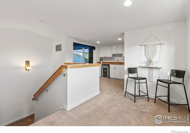 kitchen featuring light colored carpet, beverage cooler, sink, and white cabinets