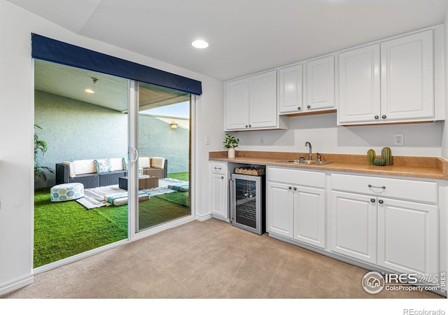 kitchen featuring sink, wine cooler, light colored carpet, and white cabinets