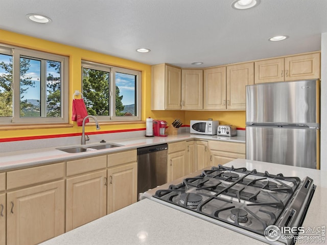 kitchen with light brown cabinets, a textured ceiling, stainless steel appliances, and sink