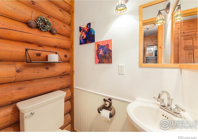 bathroom with toilet, rustic walls, and sink