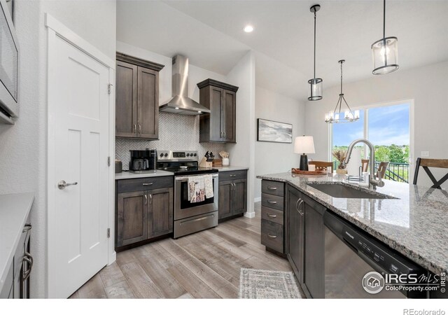 kitchen featuring wall chimney exhaust hood, stainless steel appliances, light wood-type flooring, an inviting chandelier, and sink