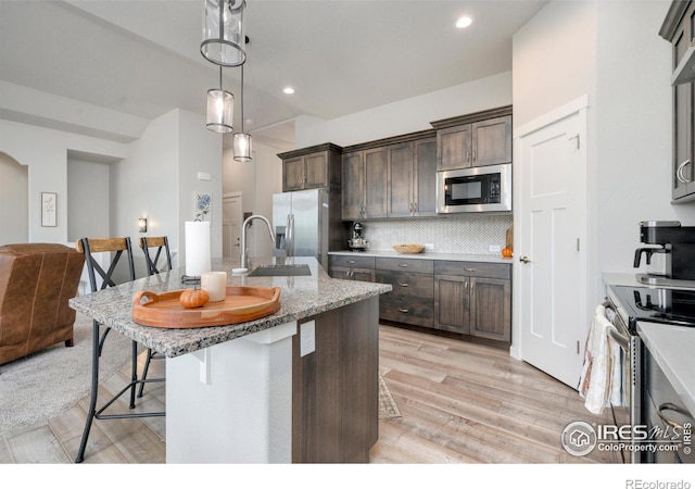 kitchen with dark brown cabinetry, a kitchen bar, decorative backsplash, appliances with stainless steel finishes, and a sink