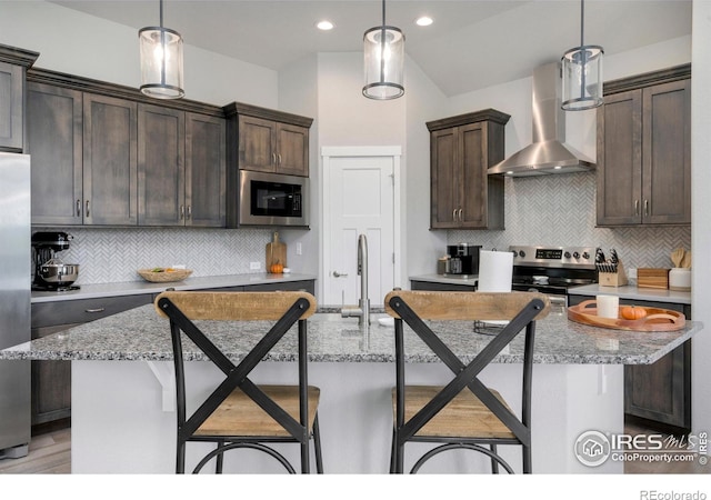 kitchen featuring wall chimney range hood, dark brown cabinetry, pendant lighting, a breakfast bar area, and stainless steel appliances
