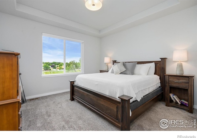 bedroom with a raised ceiling, visible vents, baseboards, and light carpet