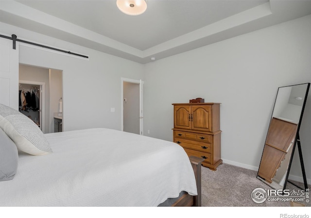 bedroom featuring a walk in closet, baseboards, a barn door, a raised ceiling, and light colored carpet