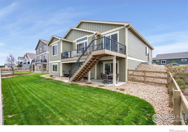 rear view of house with board and batten siding, fence, stairway, a yard, and a patio
