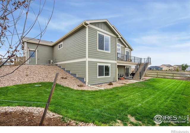 back of property with a lawn, fence, board and batten siding, a wooden deck, and stairs