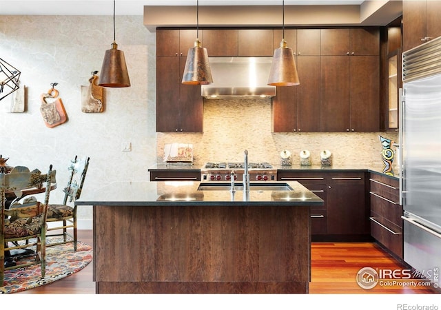 kitchen with pendant lighting, sink, an island with sink, built in fridge, and dark hardwood / wood-style flooring