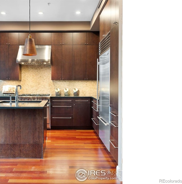 kitchen featuring pendant lighting, wood-type flooring, dark brown cabinetry, and wall chimney range hood