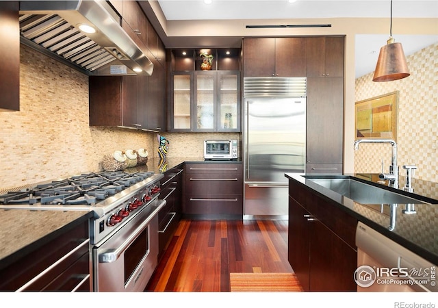 kitchen featuring premium appliances, wall chimney exhaust hood, sink, and decorative backsplash