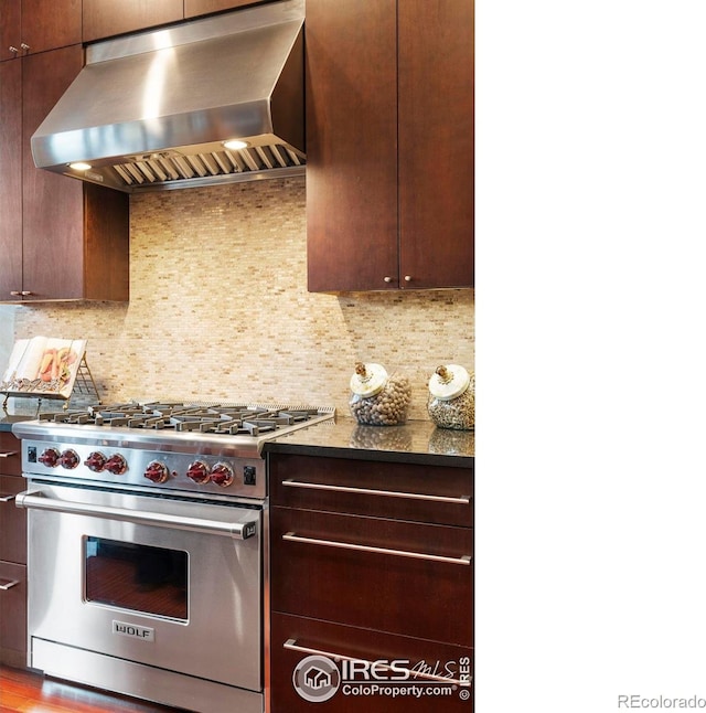 kitchen with light wood-type flooring, premium range, wall chimney range hood, backsplash, and dark stone countertops