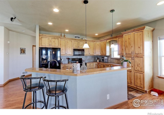 kitchen featuring backsplash, decorative light fixtures, light wood-type flooring, black appliances, and a sink