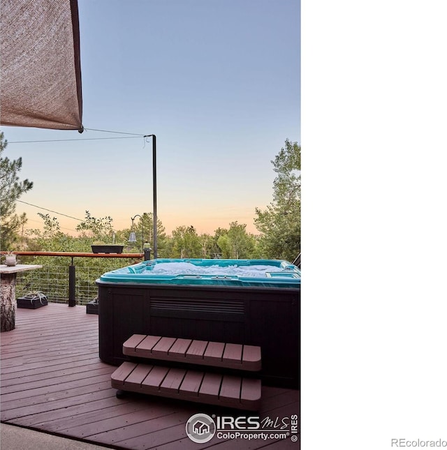 deck at dusk featuring a hot tub