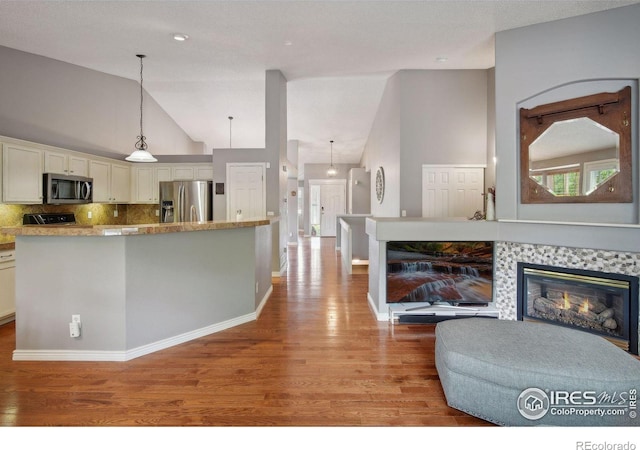 kitchen featuring pendant lighting, stainless steel appliances, a fireplace, light hardwood / wood-style floors, and decorative backsplash