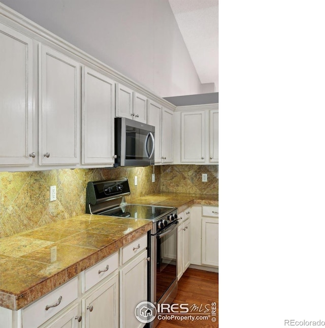 kitchen with white cabinets, appliances with stainless steel finishes, hardwood / wood-style floors, and decorative backsplash