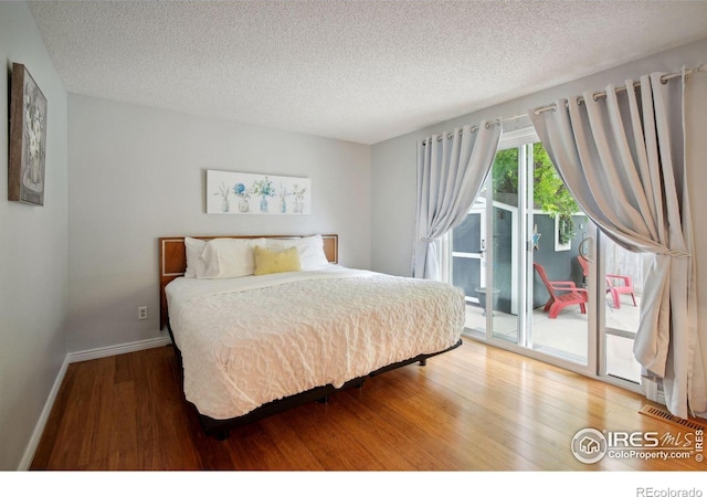 bedroom with a textured ceiling, access to exterior, and hardwood / wood-style floors