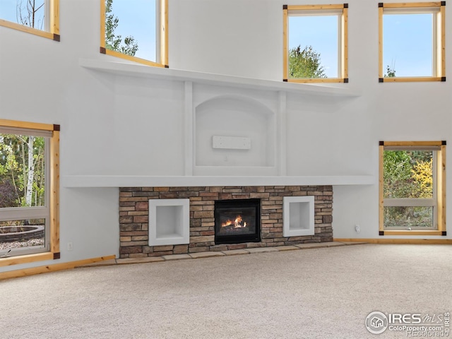 unfurnished living room featuring a stone fireplace, a towering ceiling, and a wealth of natural light