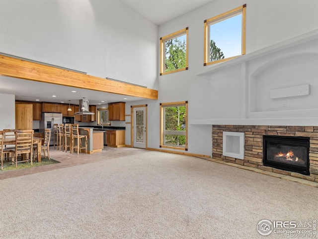 unfurnished living room featuring a stone fireplace, a high ceiling, and light carpet