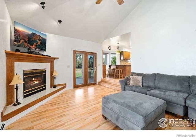 living room with high vaulted ceiling, wood finished floors, a baseboard heating unit, ceiling fan, and a premium fireplace