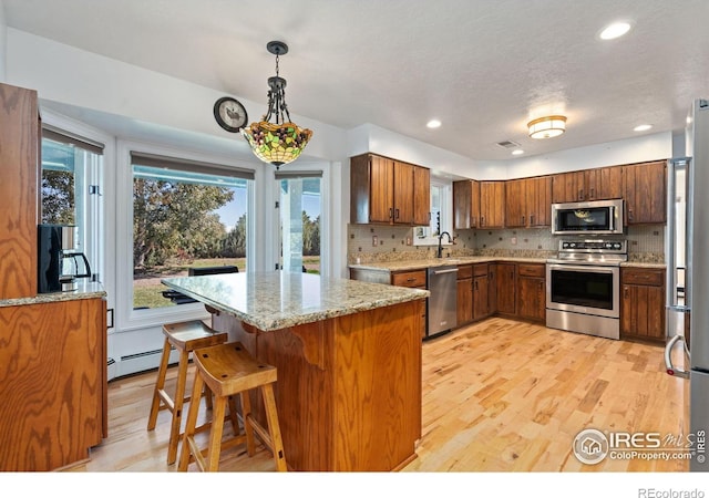 kitchen with a sink, light wood-type flooring, decorative backsplash, brown cabinetry, and appliances with stainless steel finishes