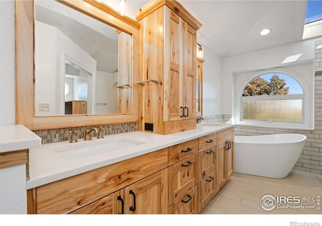 full bath featuring double vanity, tile walls, a freestanding tub, and a sink