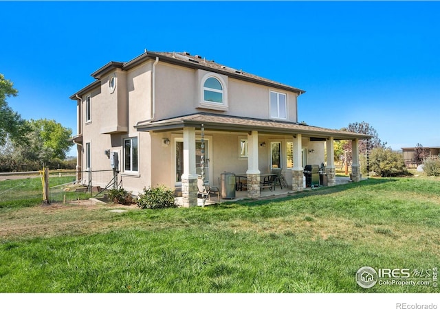 back of property with stucco siding, a patio area, a lawn, and fence