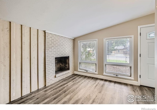 unfurnished living room featuring a brick fireplace, vaulted ceiling, and light hardwood / wood-style floors