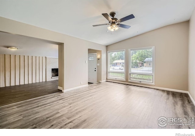 empty room featuring wood-type flooring, lofted ceiling, ceiling fan, and a fireplace