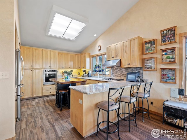 kitchen with light brown cabinets, a kitchen breakfast bar, dark hardwood / wood-style flooring, kitchen peninsula, and appliances with stainless steel finishes