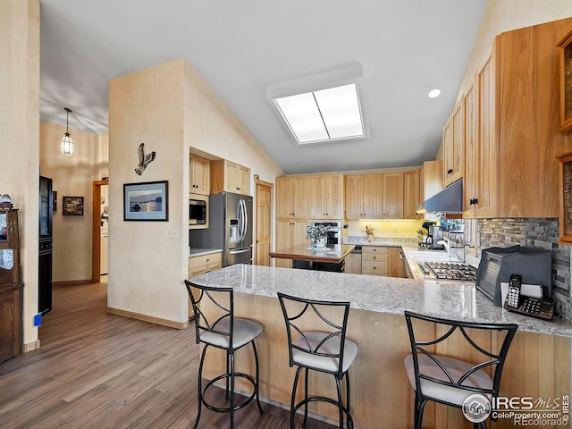 kitchen featuring pendant lighting, a kitchen breakfast bar, appliances with stainless steel finishes, light hardwood / wood-style floors, and kitchen peninsula