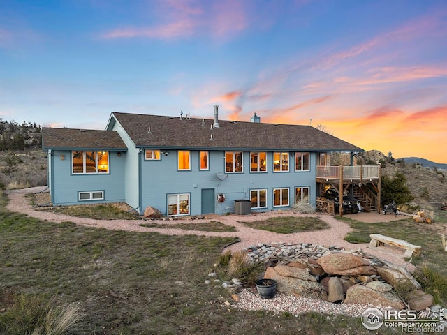 back house at dusk with central air condition unit, a wooden deck, and a yard