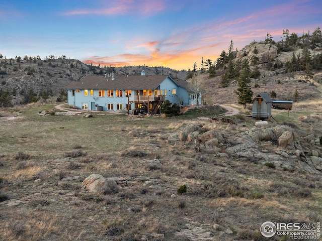 back house at dusk with a wooden deck and a storage unit