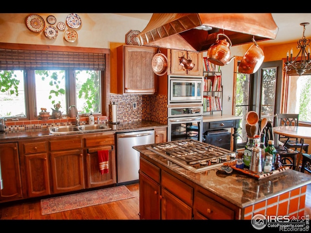 kitchen with appliances with stainless steel finishes, tasteful backsplash, pendant lighting, light hardwood / wood-style flooring, and sink