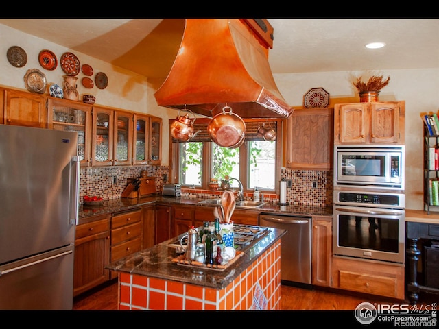 kitchen with decorative backsplash, dark wood-type flooring, a kitchen island, stainless steel appliances, and island exhaust hood