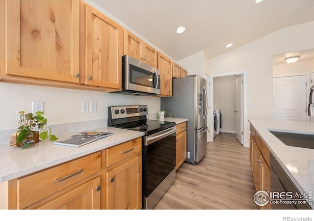 kitchen with light hardwood / wood-style flooring, washer and clothes dryer, stainless steel appliances, light stone countertops, and vaulted ceiling