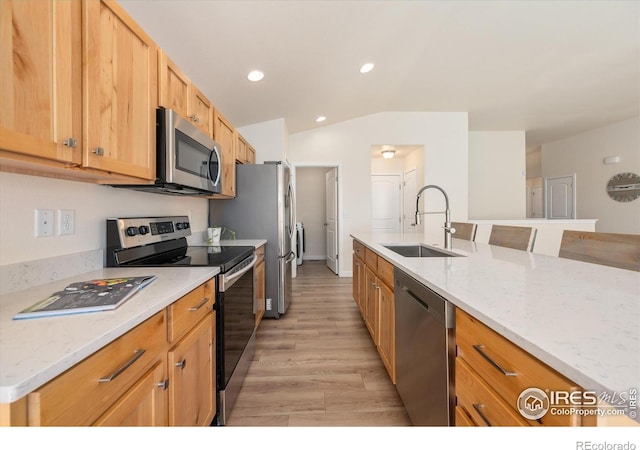 kitchen with light stone counters, lofted ceiling, sink, stainless steel appliances, and light hardwood / wood-style floors