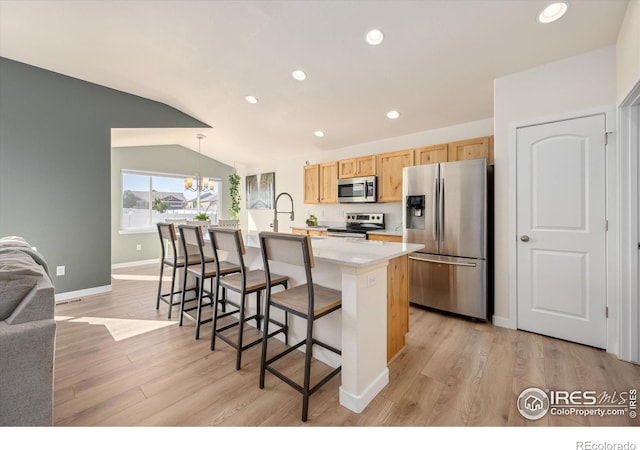 kitchen featuring pendant lighting, a kitchen island with sink, a breakfast bar area, vaulted ceiling, and appliances with stainless steel finishes