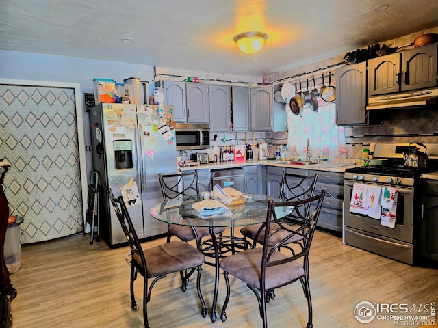 kitchen with appliances with stainless steel finishes, gray cabinetry, light wood-type flooring, sink, and backsplash