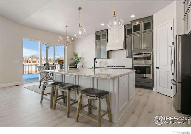 kitchen with pendant lighting, an island with sink, appliances with stainless steel finishes, a notable chandelier, and light wood-type flooring