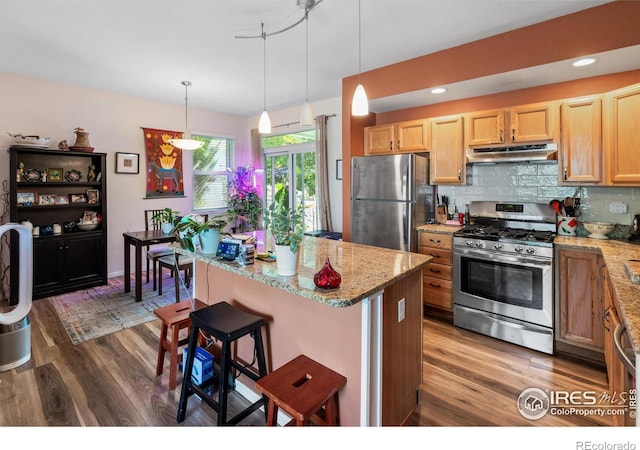 kitchen with pendant lighting, a kitchen bar, appliances with stainless steel finishes, and dark hardwood / wood-style floors