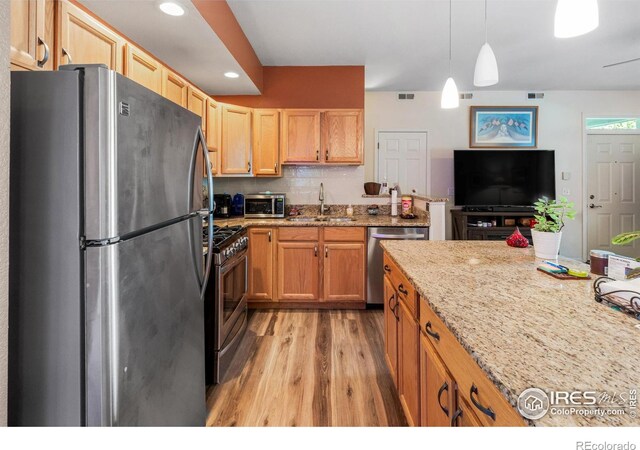 kitchen featuring light stone counters, sink, hanging light fixtures, light hardwood / wood-style flooring, and appliances with stainless steel finishes