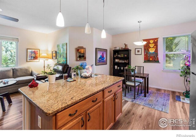 kitchen featuring light wood-type flooring, hanging light fixtures, a center island, and light stone counters