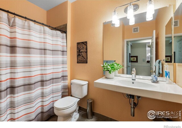 bathroom featuring toilet, a shower with shower curtain, and sink