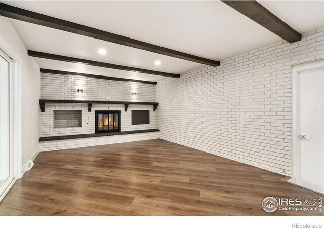 unfurnished living room with beamed ceiling, brick wall, hardwood / wood-style flooring, and a fireplace