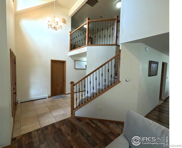 stairs with visible vents, wood finished floors, a high ceiling, baseboard heating, and a chandelier