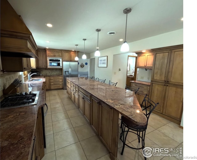 kitchen featuring a large island, stainless steel appliances, a kitchen bar, a sink, and light tile patterned flooring