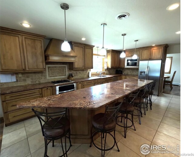 kitchen with light tile patterned floors, premium range hood, a kitchen island, decorative backsplash, and stainless steel fridge